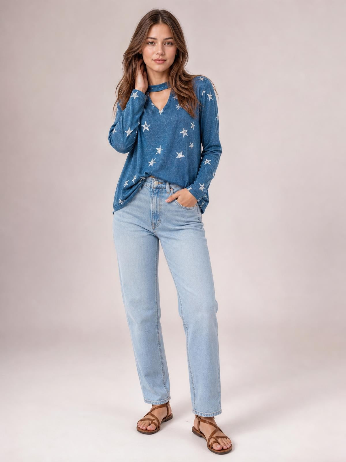 Model wears a blue star-print long sleeve T-shirt with a choker-style cutout neckline and relaxed silhouette, posing with one hand at her neck.