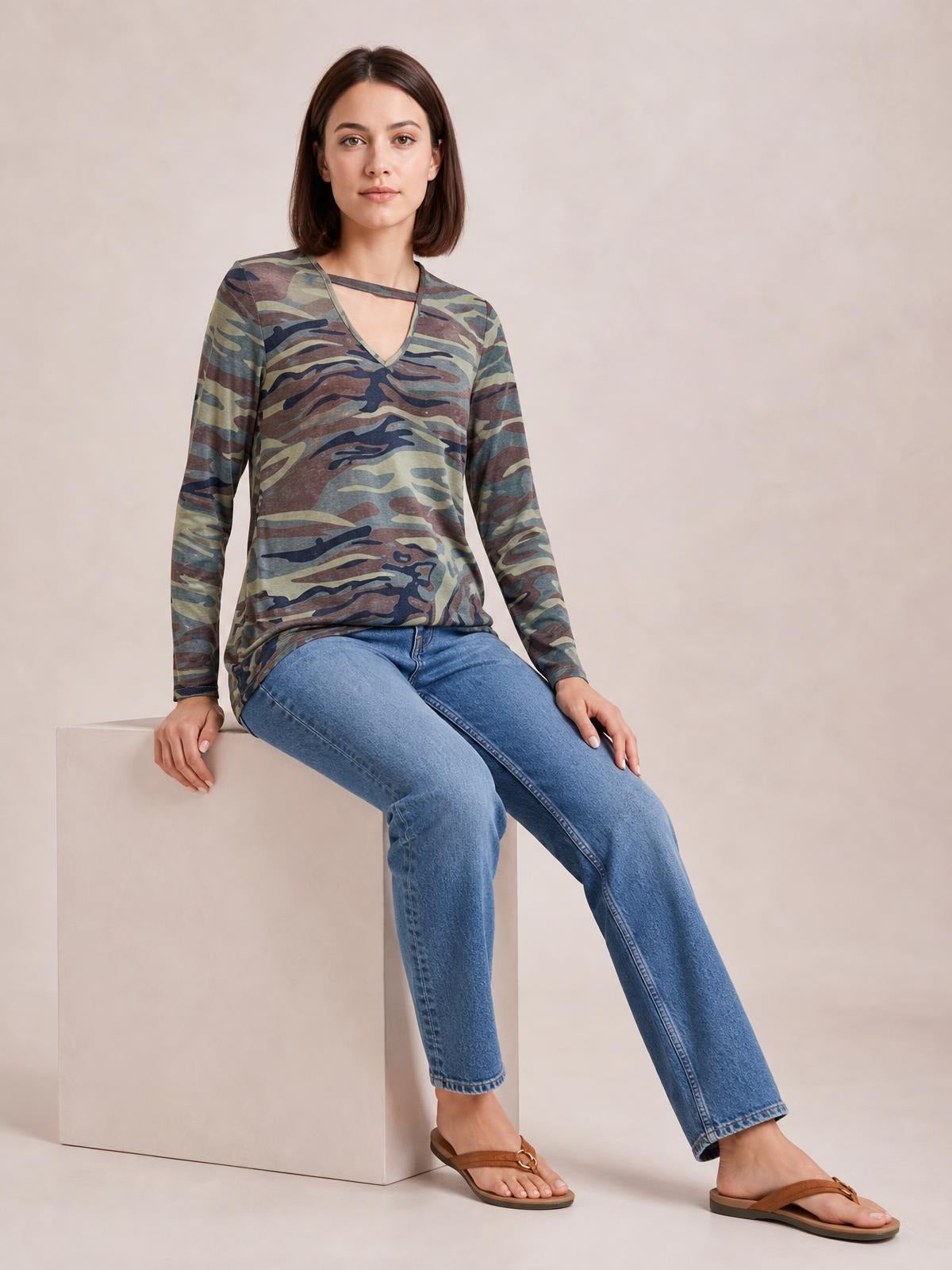 Seated model wears a camouflage cutout long-sleeve T-shirt with a fitted silhouette, sheer-looking neckline opening, and relaxed hem over blue jeans.