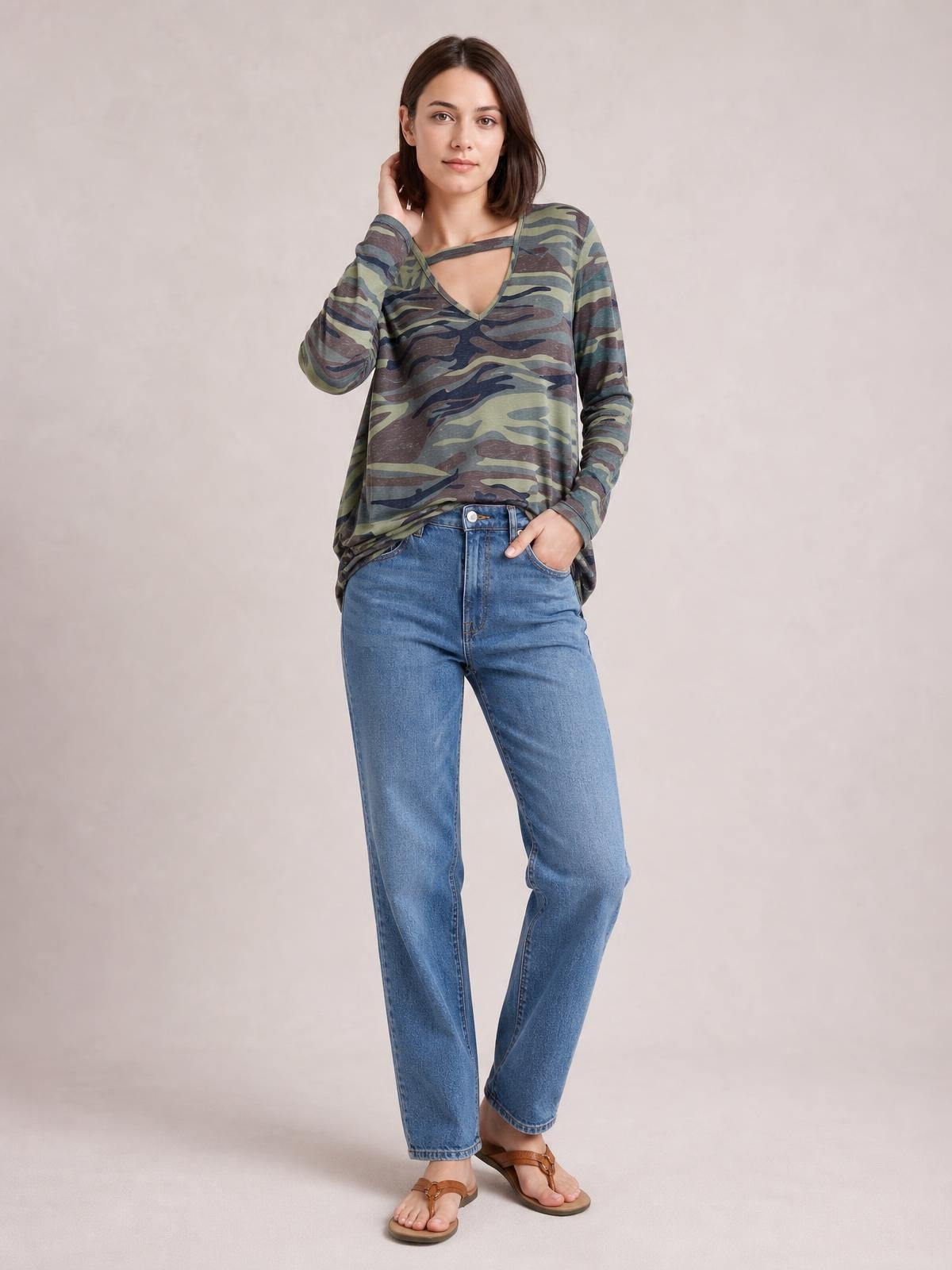 Model wearing a camouflage cutout round neck long sleeve T-shirt with a relaxed silhouette, standing with one hand in her jeans pocket.