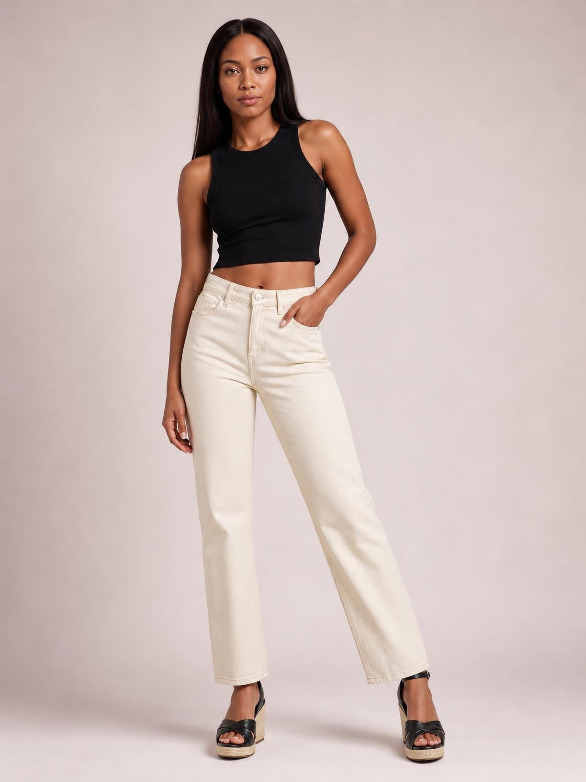 Model wears a black cutout round neck tank with a fitted cropped silhouette, sleeveless construction, and moderate stretch while posing with one hand in her pocket.