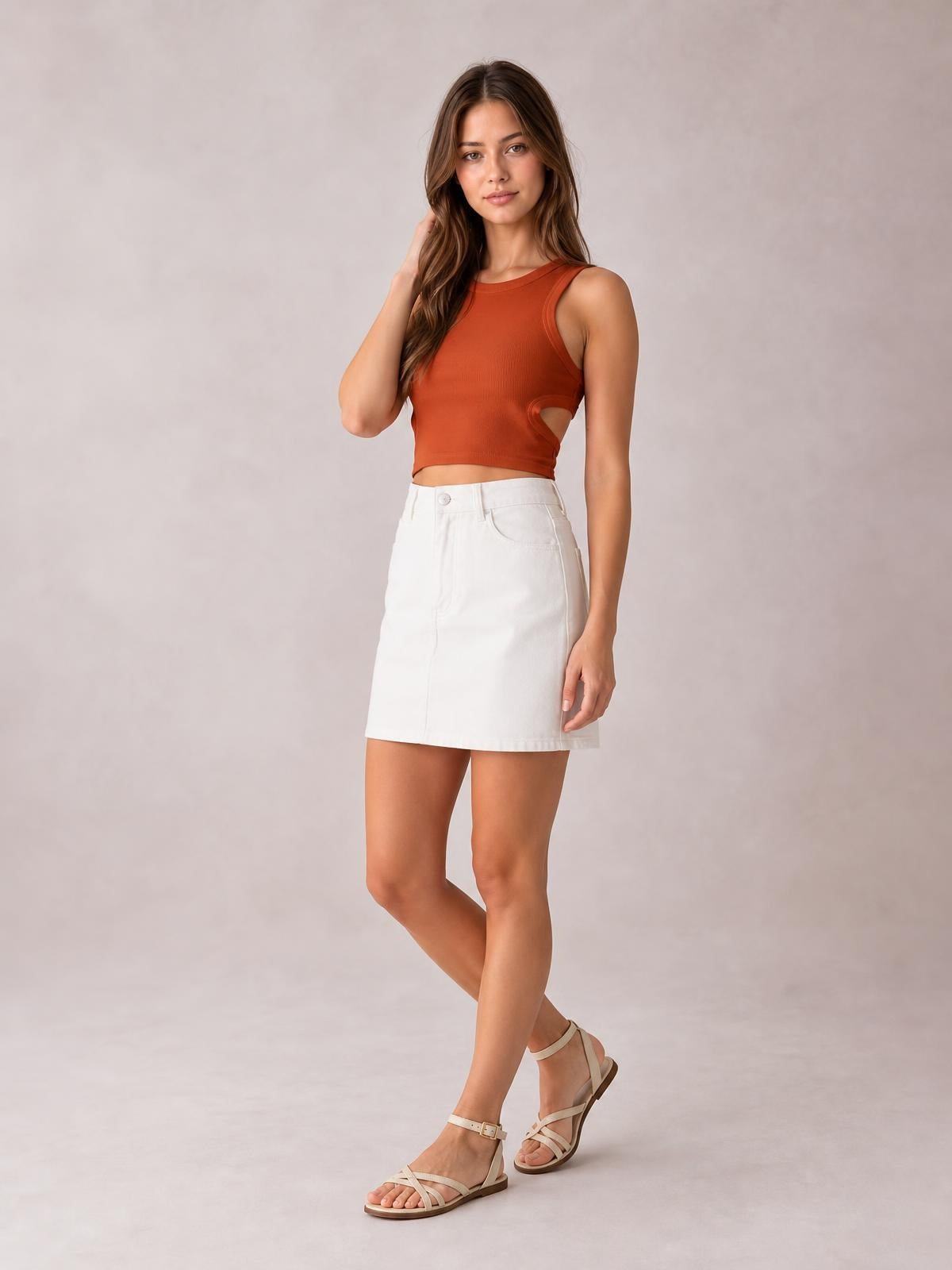 Model poses in a rust cutout round neck tank with a fitted cropped silhouette, wide shoulder straps, and side cutout at the waist.