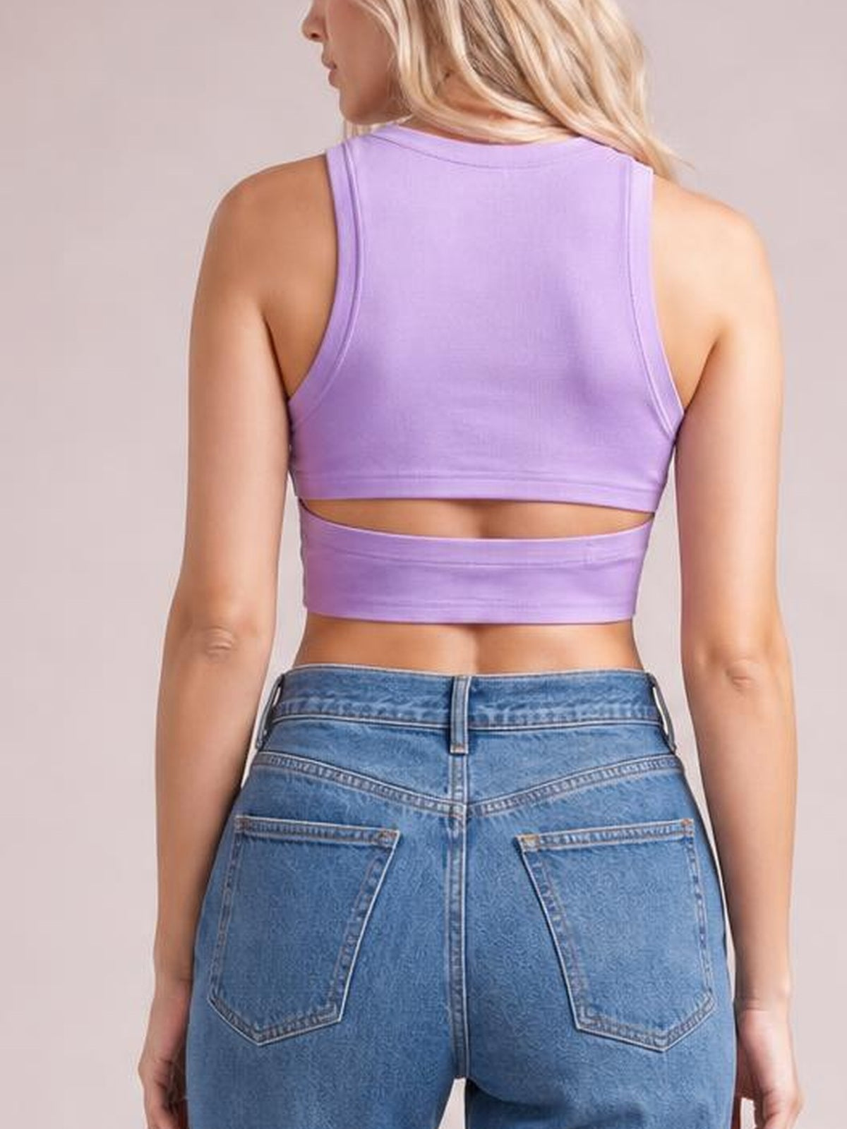 A model stands facing away in a lavender cutout round neck tank with sleeveless styling, a fitted cropped silhouette, and a horizontal back cutout.