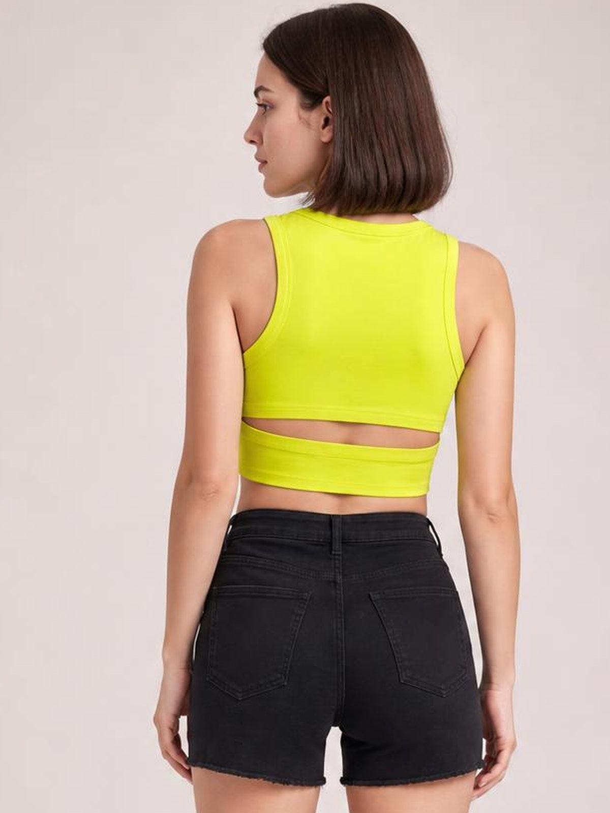 Model shown from behind in a neon yellow cutout round neck tank with a sleeveless silhouette, fitted crop length, and horizontal mid-back opening.
