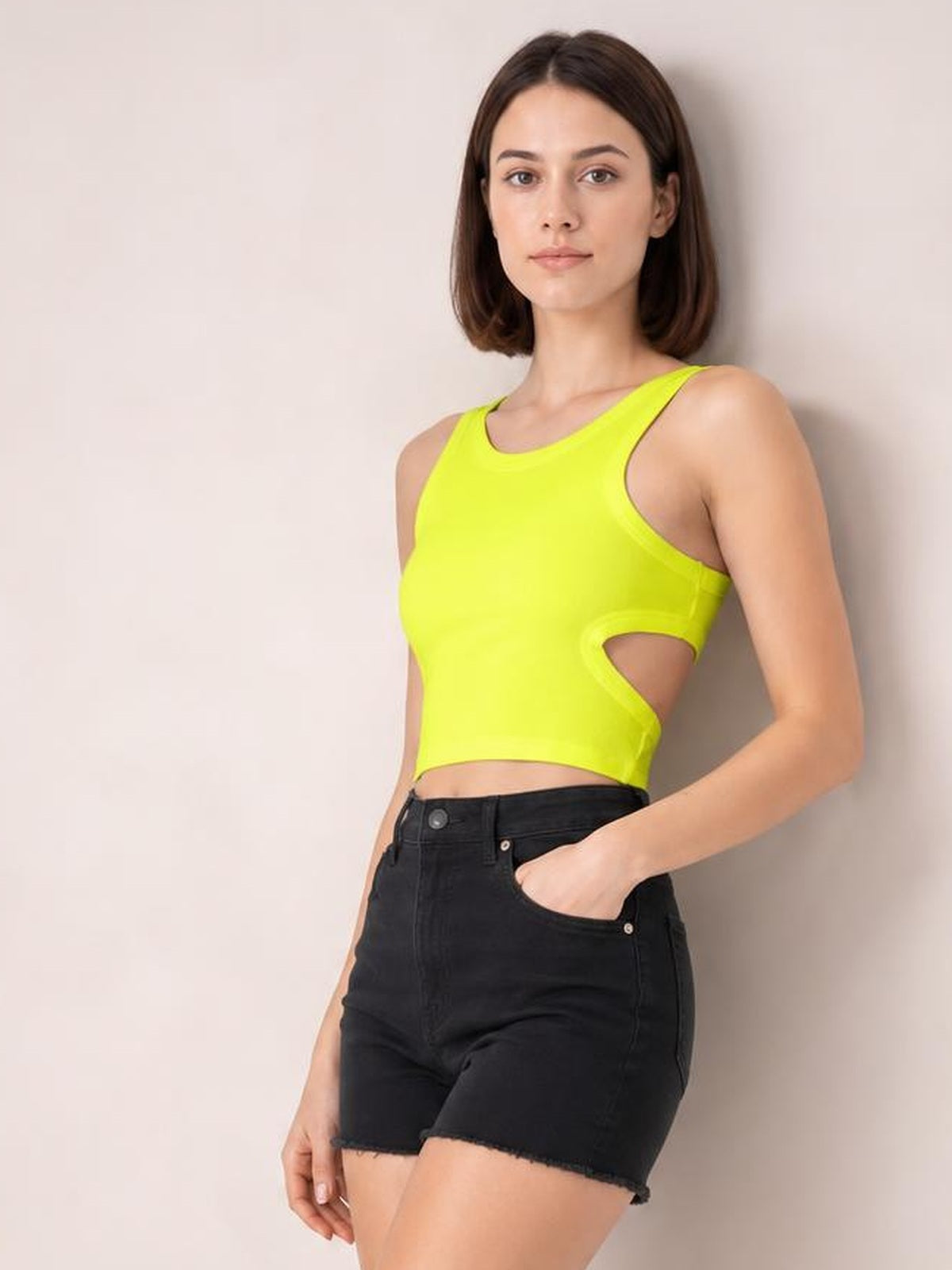 A model poses in a neon yellow cutout round neck tank with a fitted cropped silhouette, wide shoulder straps, and a side waist opening.