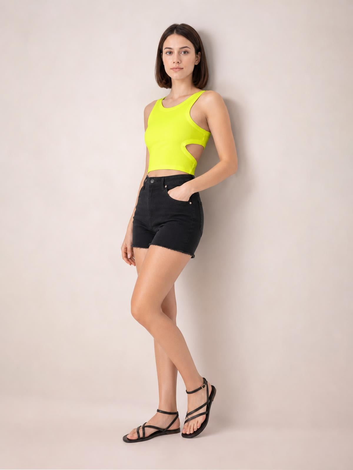 Model poses in a bright yellow cutout round neck tank with a fitted cropped silhouette, paired with black high-waisted shorts.