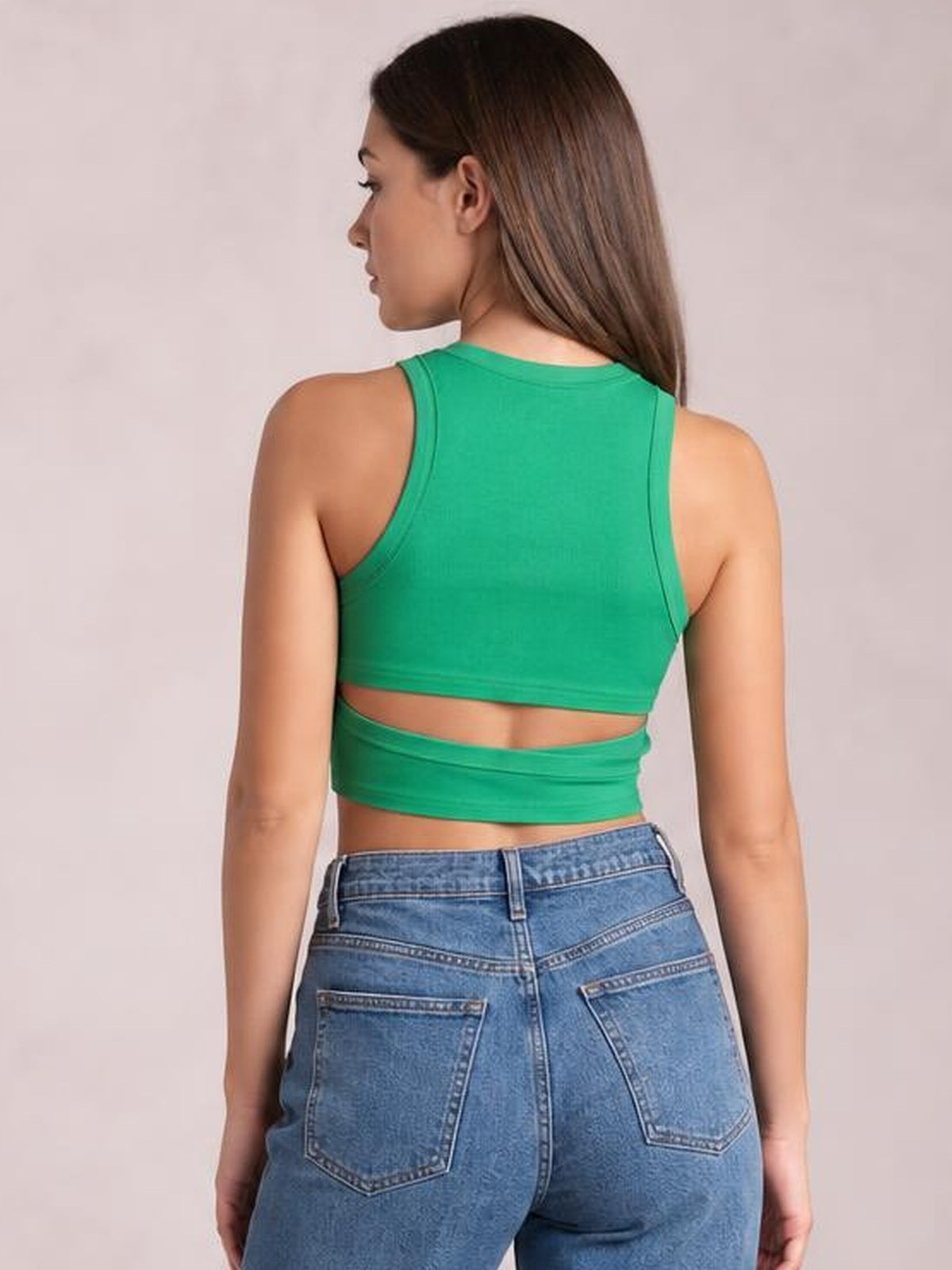 A model turns away to show a fitted bright green cutout round-neck tank with wide shoulder straps, cropped silhouette, and a horizontal waist opening.