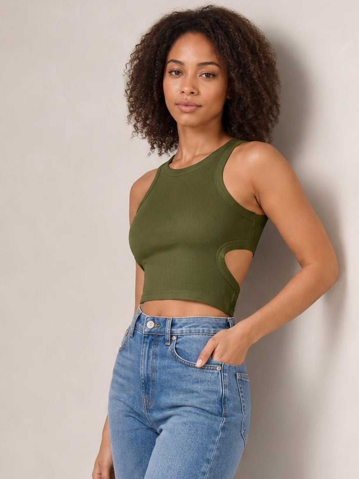 Model poses in an olive green cutout round neck tank with wide shoulder straps, sleeveless styling, and a fitted cropped silhouette.