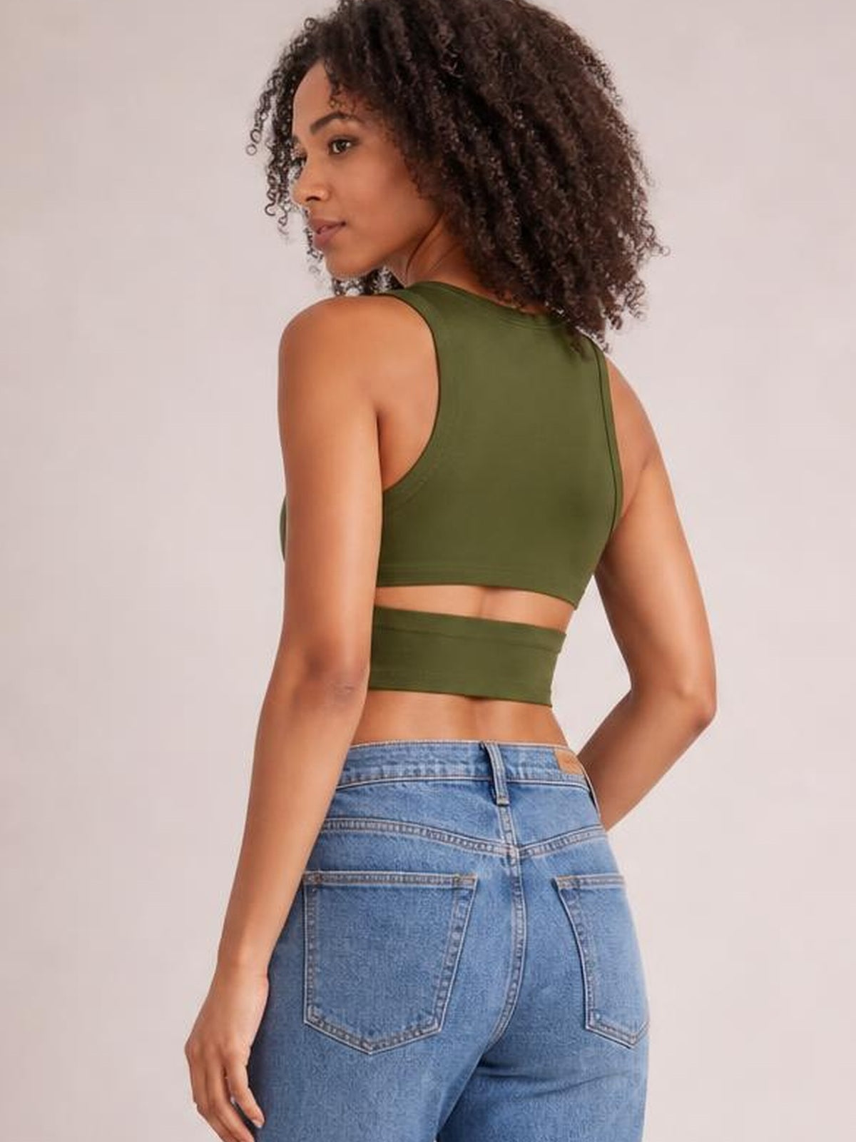 Model looks over her shoulder in a fitted olive green cutout round neck tank with wide straps, cropped silhouette, and moderate stretch.