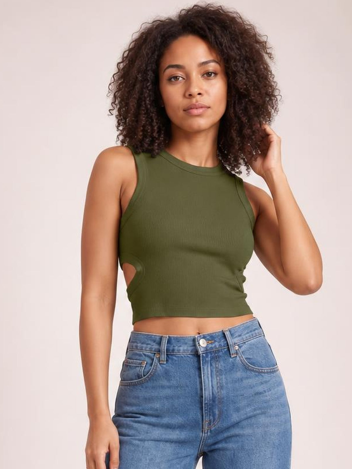 Model poses in a fitted olive green cutout round neck tank with wide shoulder straps and a cropped silhouette, paired with blue jeans.