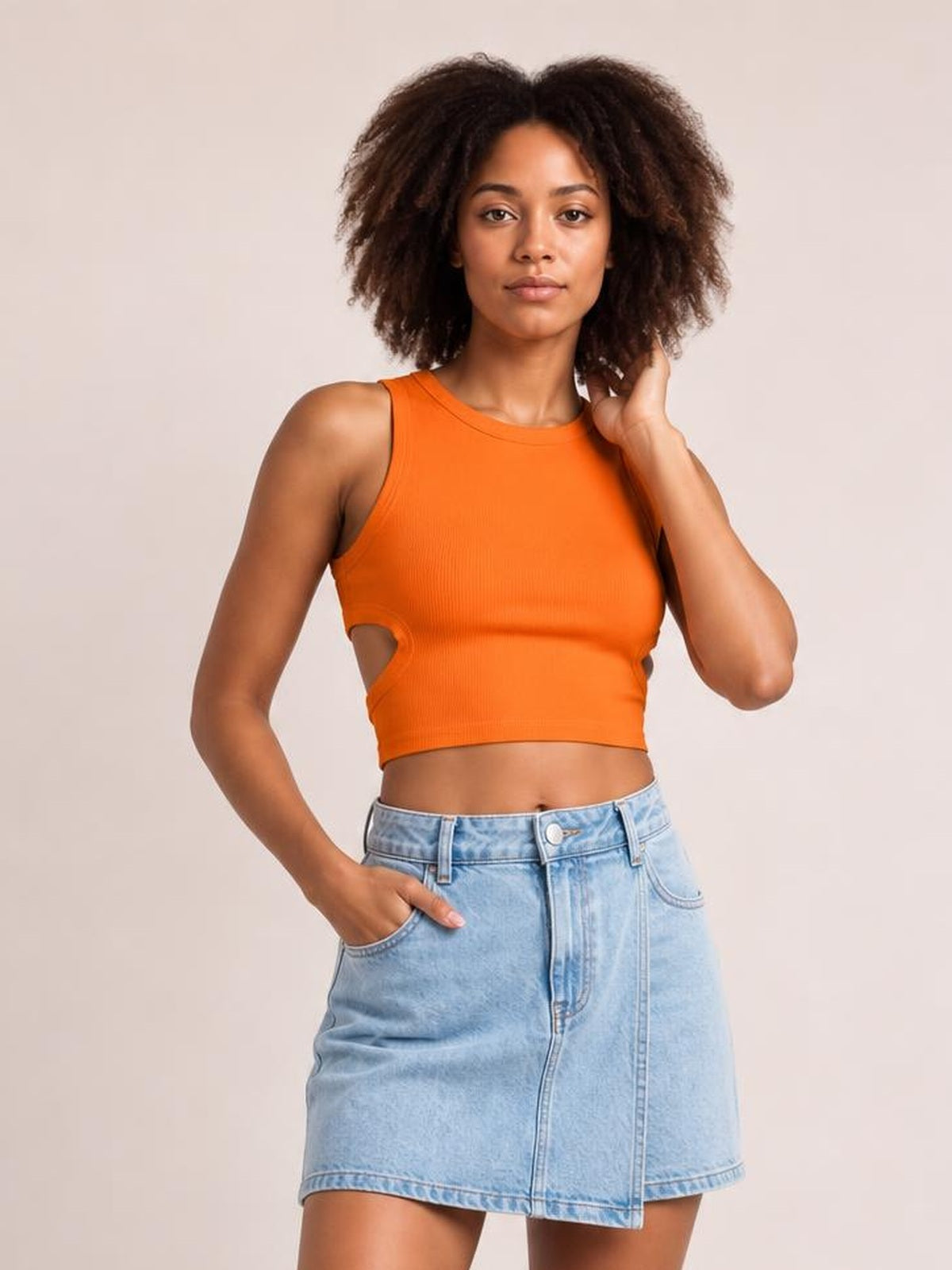 Model poses in an orange cutout round neck tank with a fitted cropped silhouette, wide shoulder straps, and side cutouts.