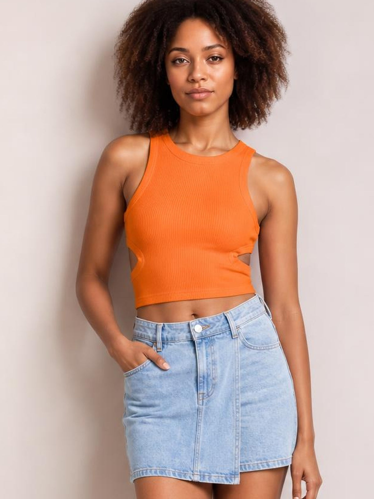 Model wearing an orange cutout round neck tank with a fitted ribbed silhouette and sleeveless construction, paired with a light wash denim skirt.