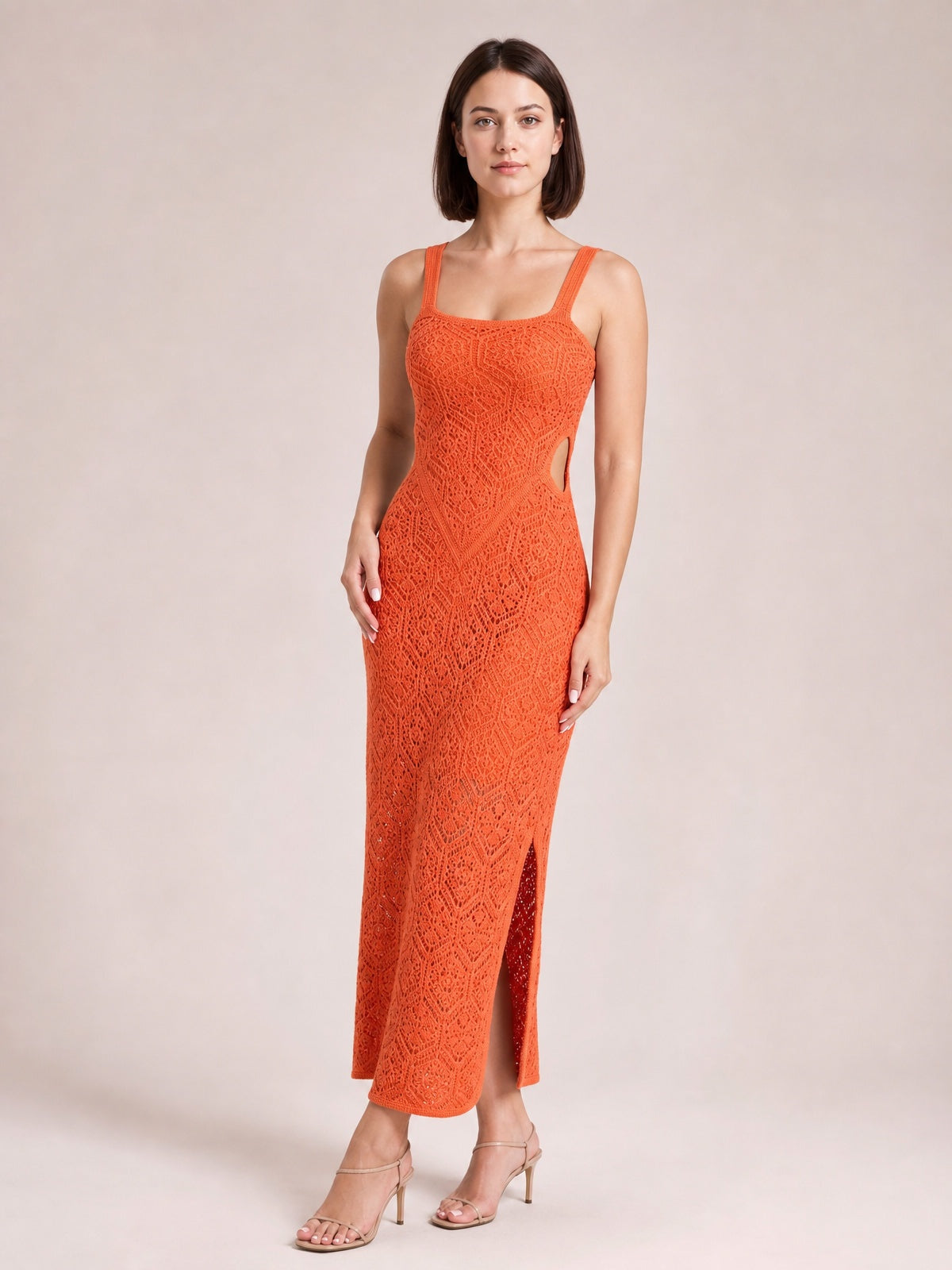 Model stands in an orange maxi tank dress with slim straps, intricate eyelet texture, a body-skimming silhouette, curved side cutout, and long side slit.