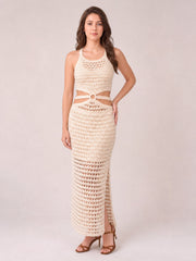 Model poses in a cream sleeveless sweater dress with a round neck, open-knit texture, waist cutouts, fitted midi silhouette, and side slit.