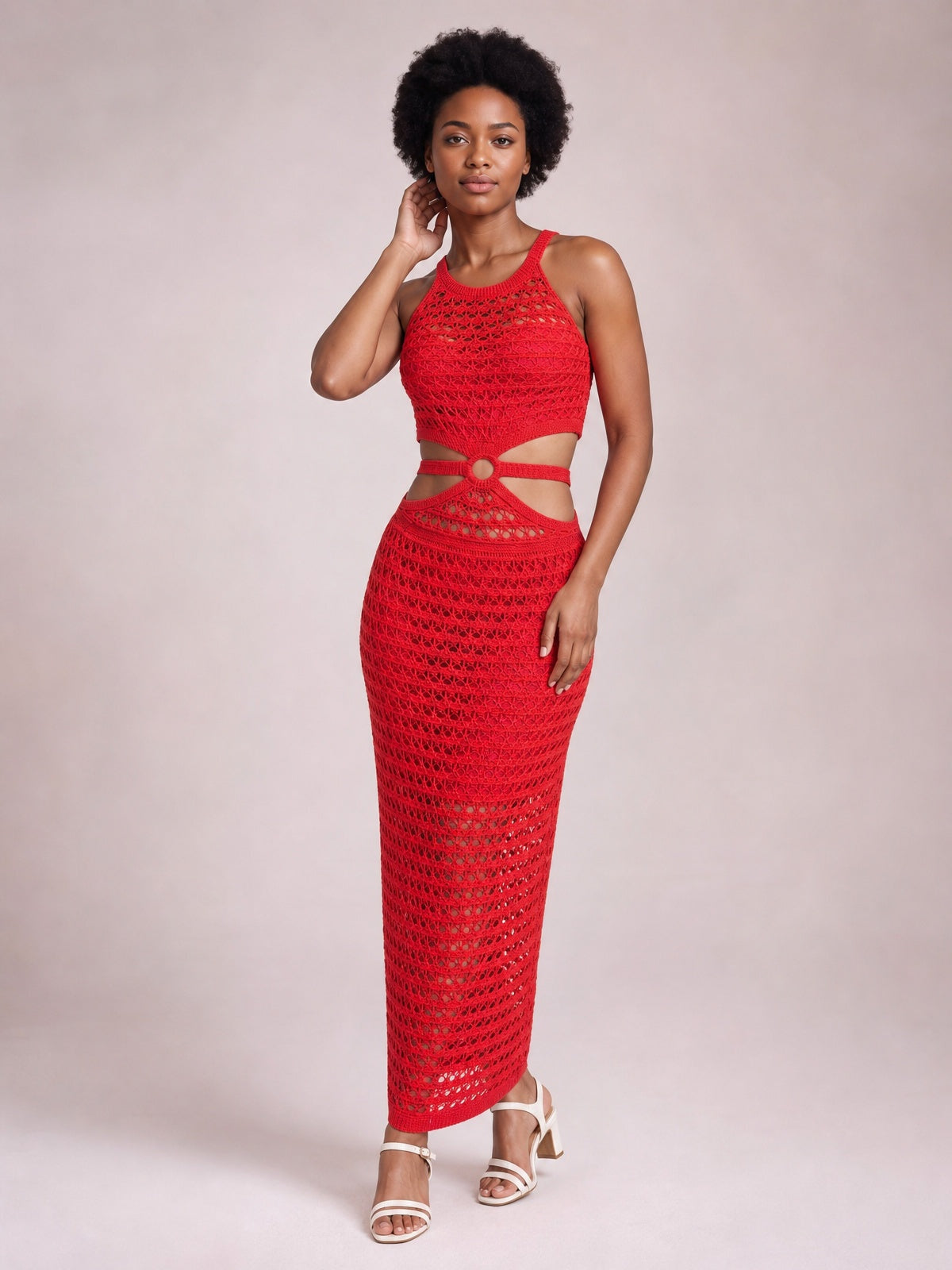 A model poses in a red sleeveless round-neck sweater dress with open-knit texture, waist cutouts, a fitted midi silhouette, and a side slit.