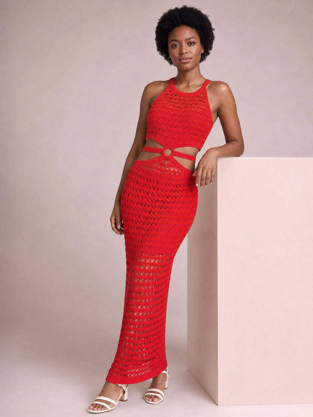 A model poses in a red sleeveless round-neck sweater dress with open-knit texture, waist cutouts, and a fitted floor-length silhouette.