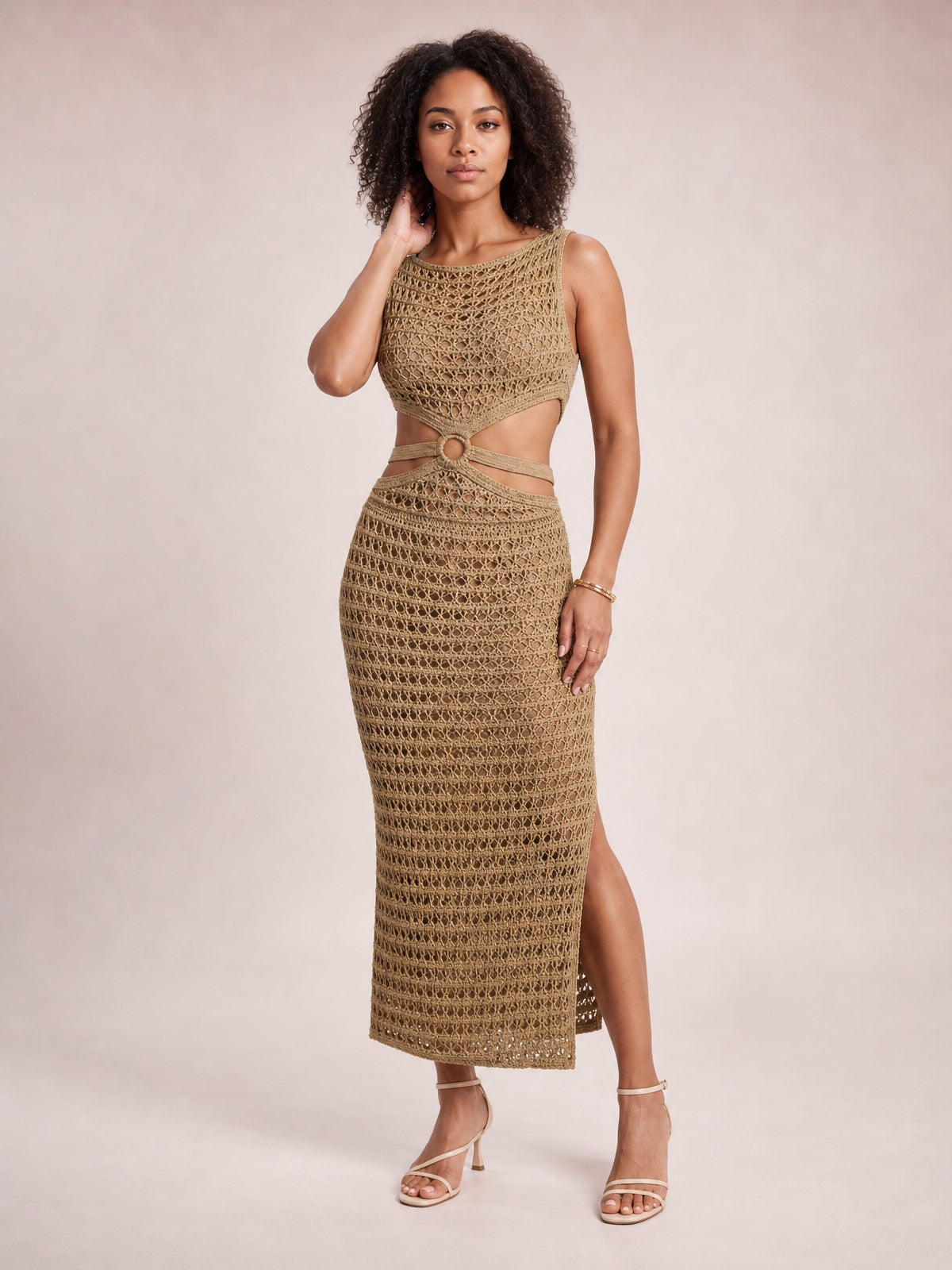Model poses in a tan open-knit sweater dress with a round neck, sleeveless fitted midi silhouette, waist cutout, ring detail, and side slit.