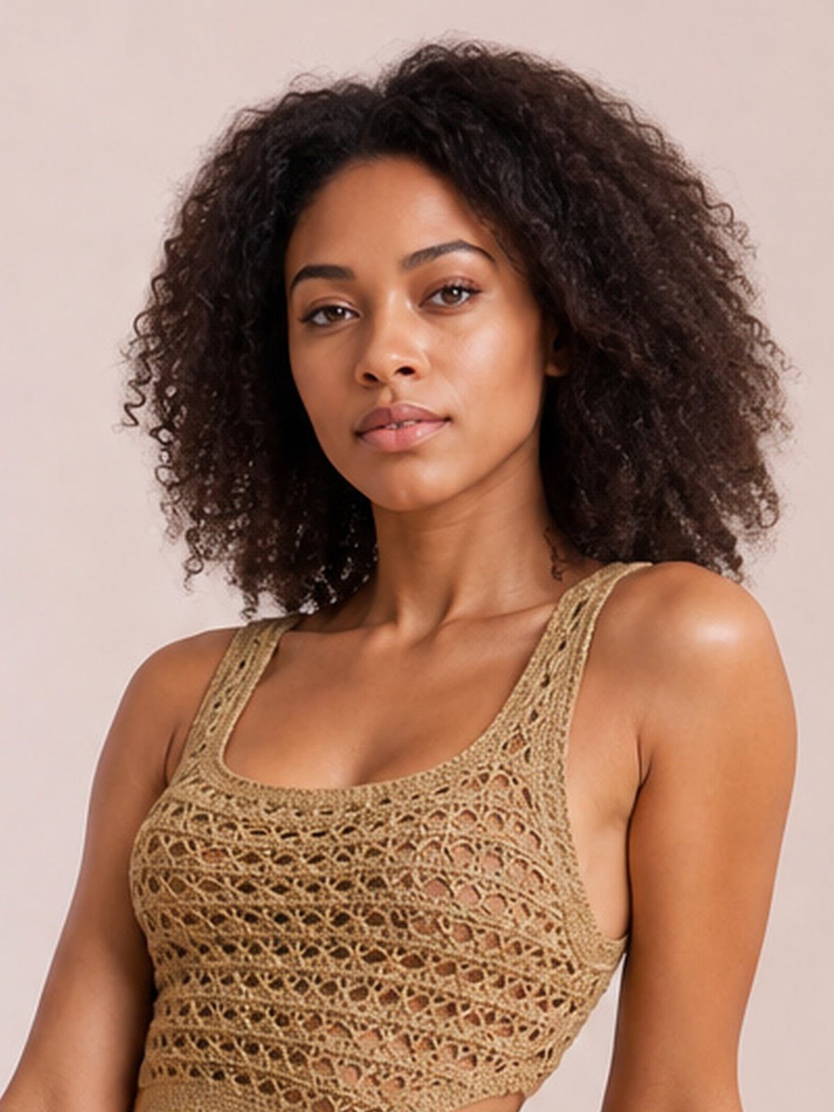 A model wears a tan sleeveless sweater dress with a rounded neckline, fitted silhouette, and textured open-knit construction, posed with a slight lean.