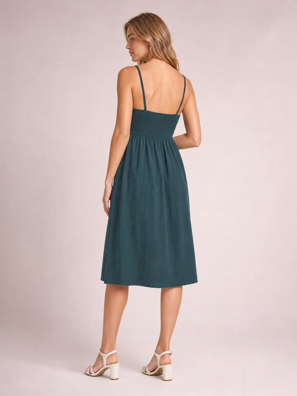 Model shown from the back in a teal cami dress with slender straps, smocked bodice, gathered waist, and flowing below-the-knee A-line skirt.