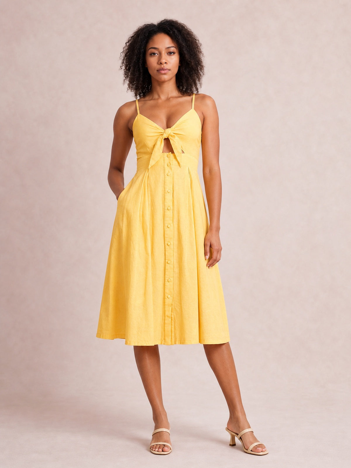 Model in a yellow cami dress with a tied sweetheart neckline, front cutout, decorative buttons, and a softly flared below-the-knee A-line skirt.