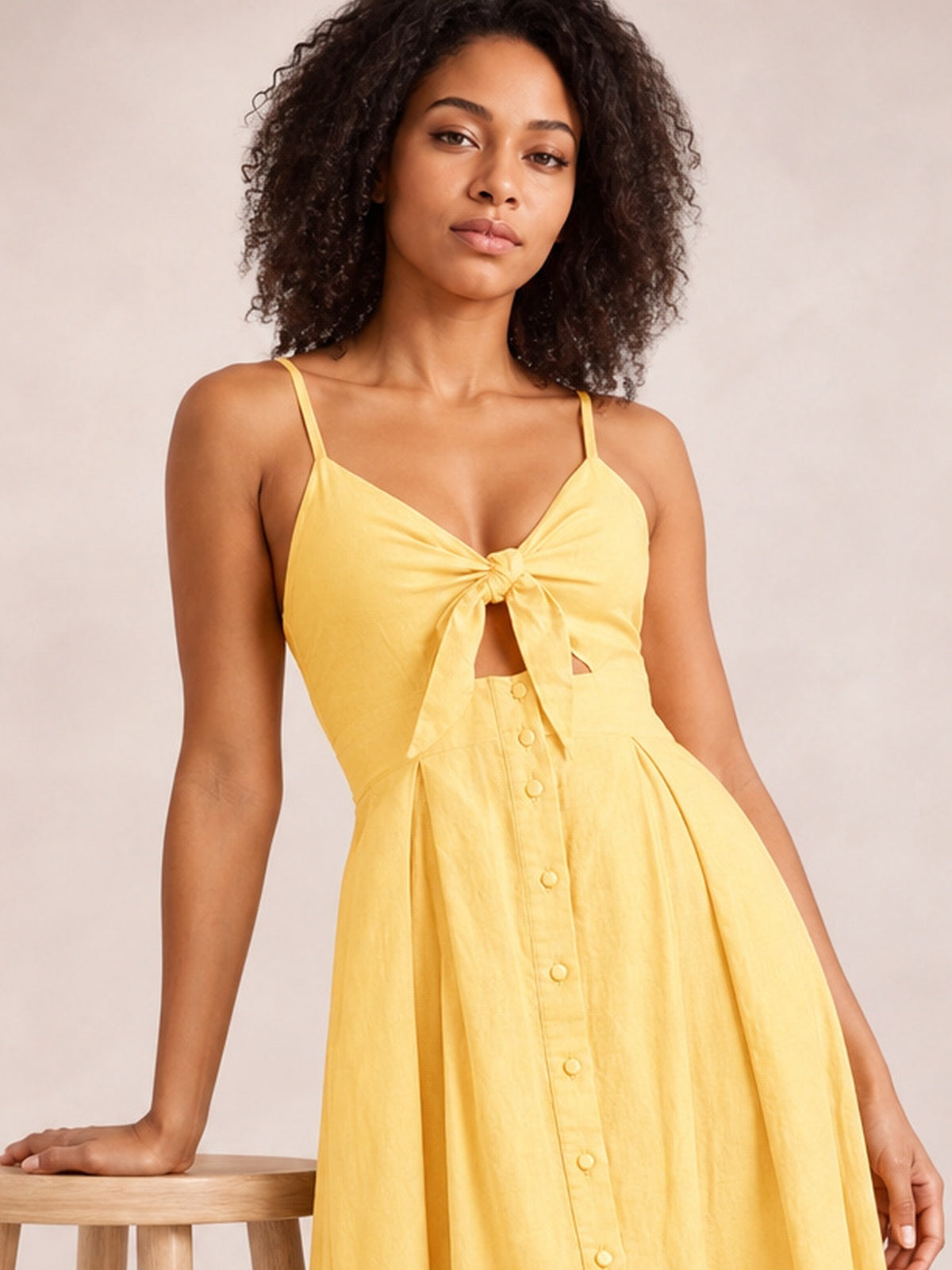A model poses in a yellow cami dress with slender straps, a tied sweetheart bodice and cutout, decorative front buttons, and a flowing A-line skirt.