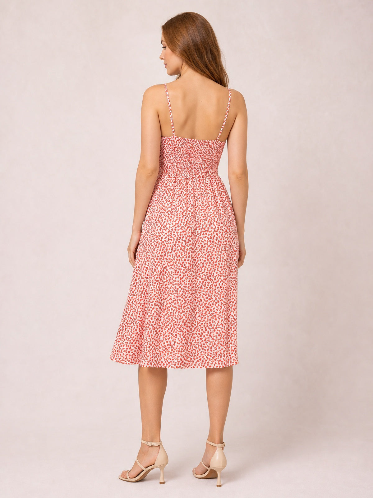 Model stands facing away in a white and coral patterned cami dress with slender straps, a smocked back, fitted waist, and below-the-knee A-line skirt.