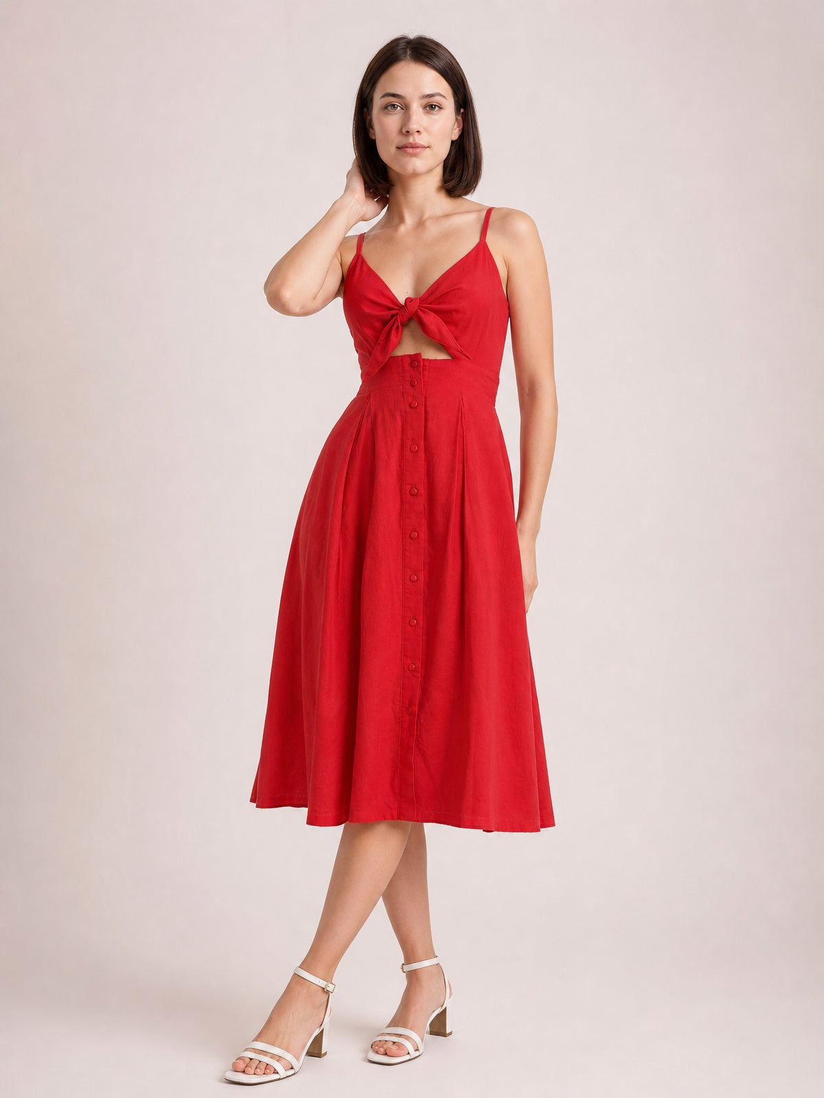 Model poses in a red cami dress with slender straps, a tied cutout bodice, decorative front buttons, and a softly full A-line skirt below the knee.