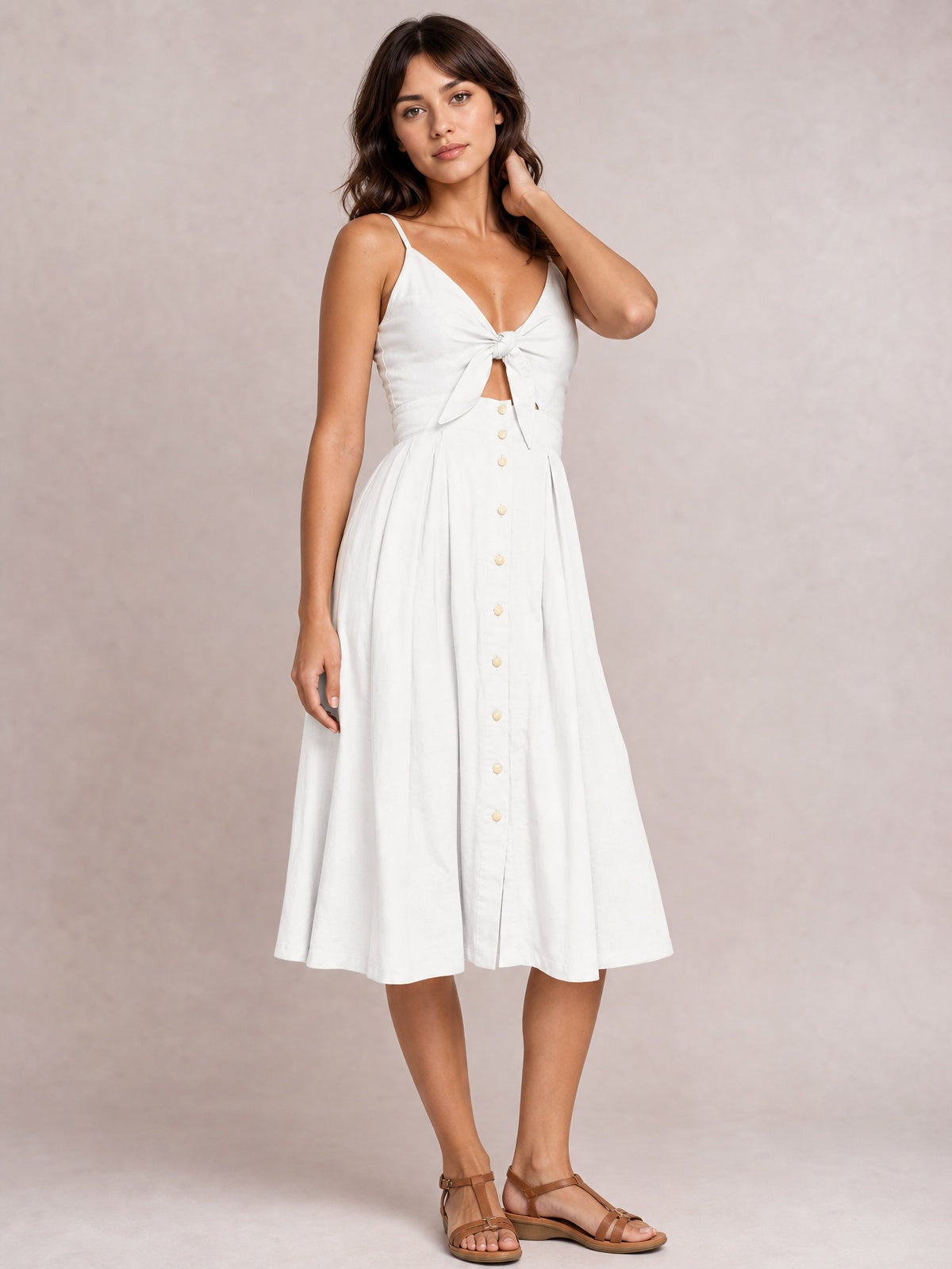 A model poses in a white cami dress with slender straps, sweetheart neckline, tied cutout bodice, decorative front buttons, and a flowing below-the-knee A-line skirt.