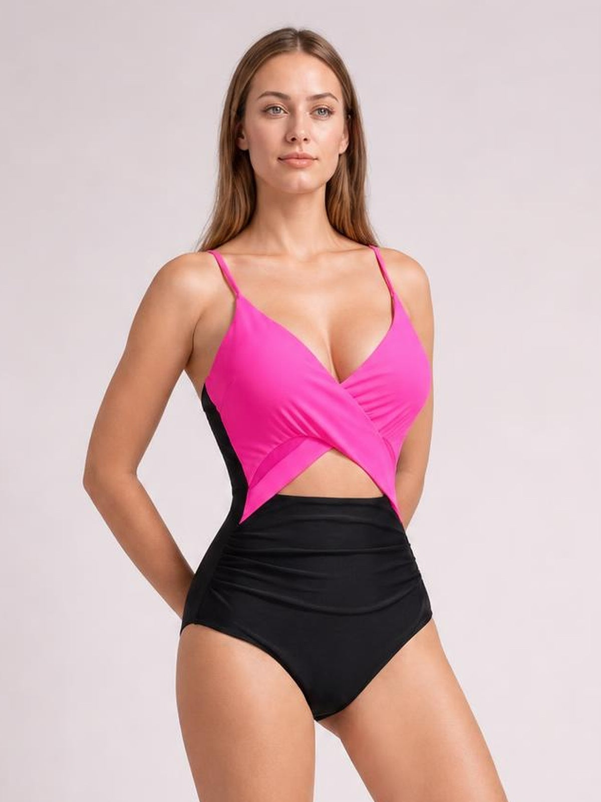 A model poses in a pink and black cutout spaghetti strap one-piece swimsuit with a crossover bodice, midriff opening, and high-rise brief silhouette.