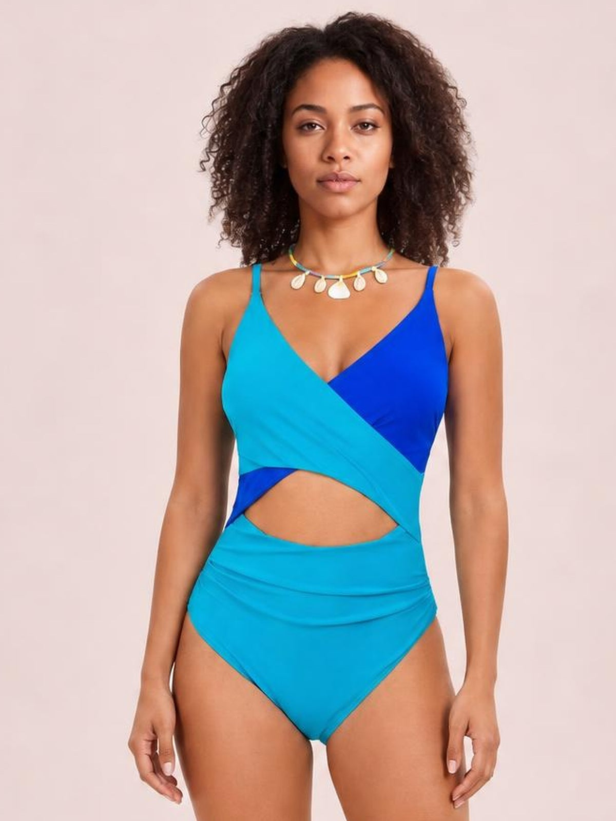 Front-facing model wears a turquoise and blue color-block one-piece swimsuit with spaghetti straps, a wrap-style bodice, and a waist cutout.