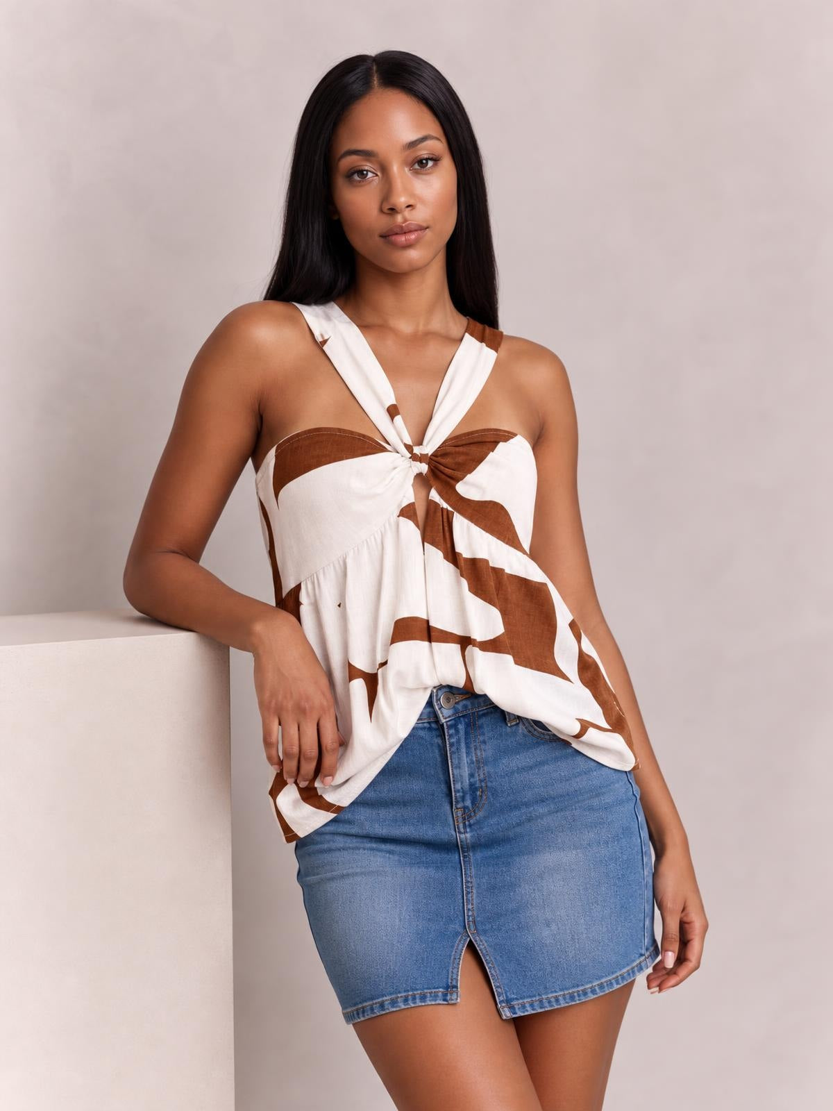 A model wears a white and brown printed cutout sweetheart-neck cami with twisted halter straps, a knotted center, and a softly ruched, flowing silhouette.