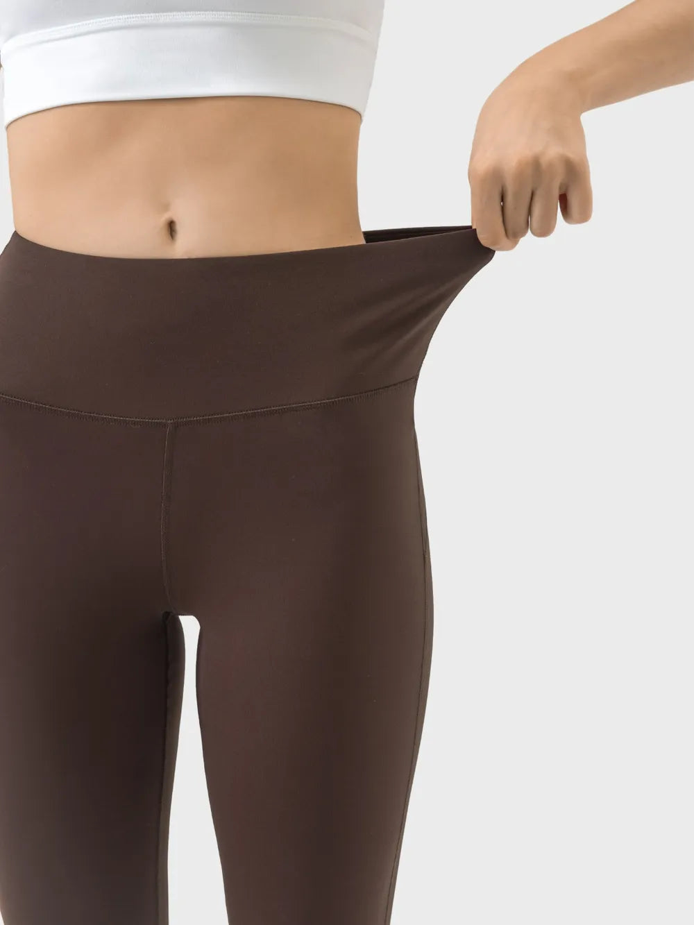 Close-up of a model wearing brown high-waist active pants with a fitted silhouette, stretch waistband, and visible front and hip seams.