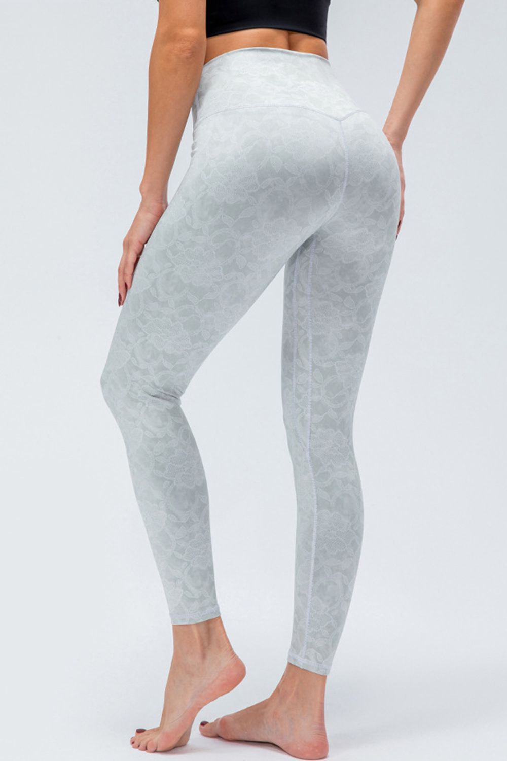 Model poses in light gray printed active leggings with a wide waistband, slim-fit silhouette, full-length legs, and one foot lifted behind.