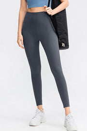Model wears solid charcoal slim-fit long sports leggings with a wide waistband and visible front seam, standing in a relaxed pose.