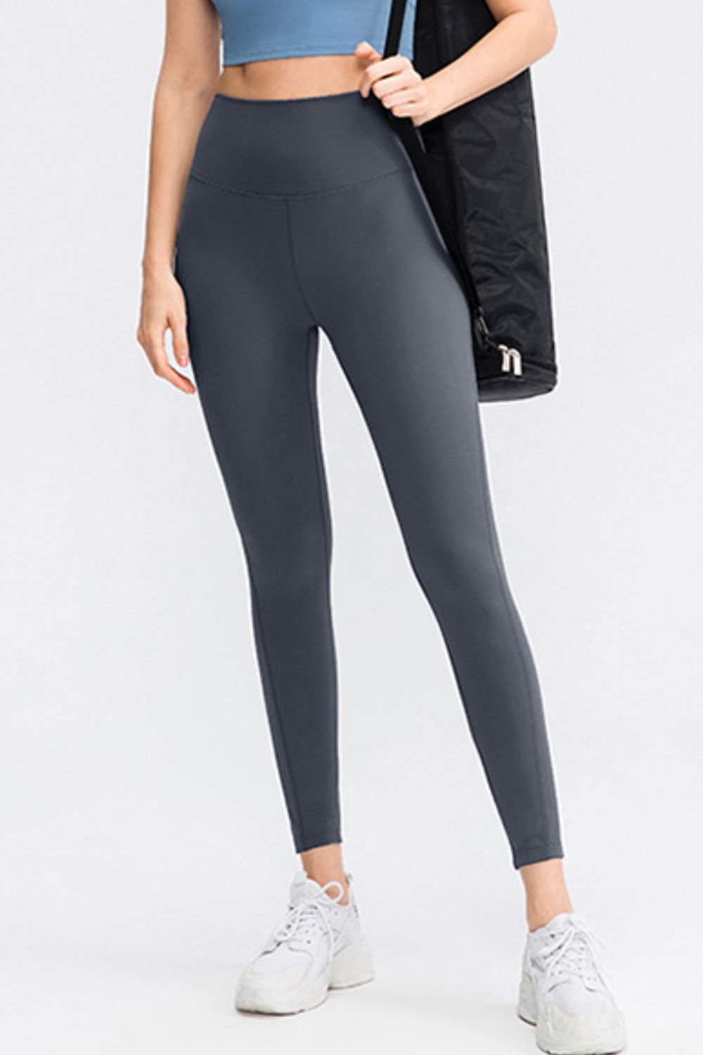 Model wears solid charcoal slim-fit long sports leggings with a wide waistband and visible front seam, standing in a relaxed pose.