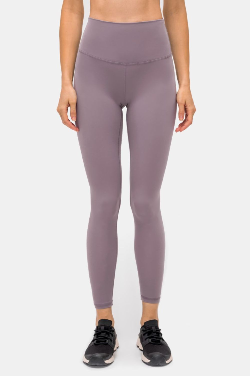 Model stands facing forward in mauve high-rise sports leggings with a slim, ankle-length silhouette, matte stretch fabric, and visible seamed waistband construction.