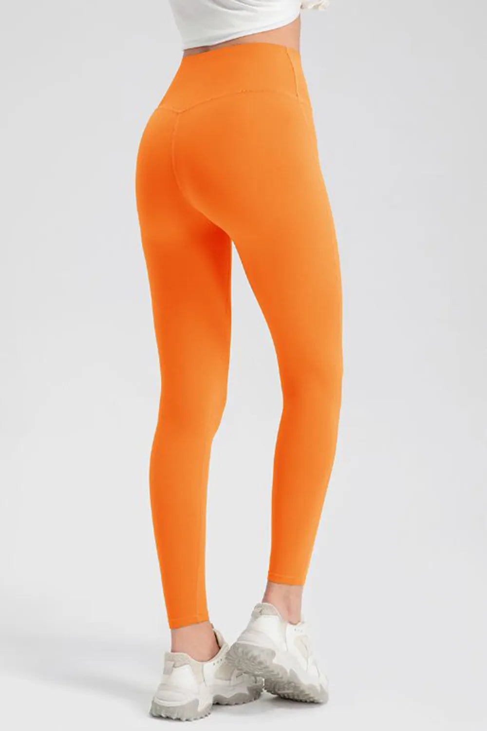 Model shown from behind in bright orange high-waist skinny active pants with a smooth fitted silhouette, ankle-length hems, and stretch construction.