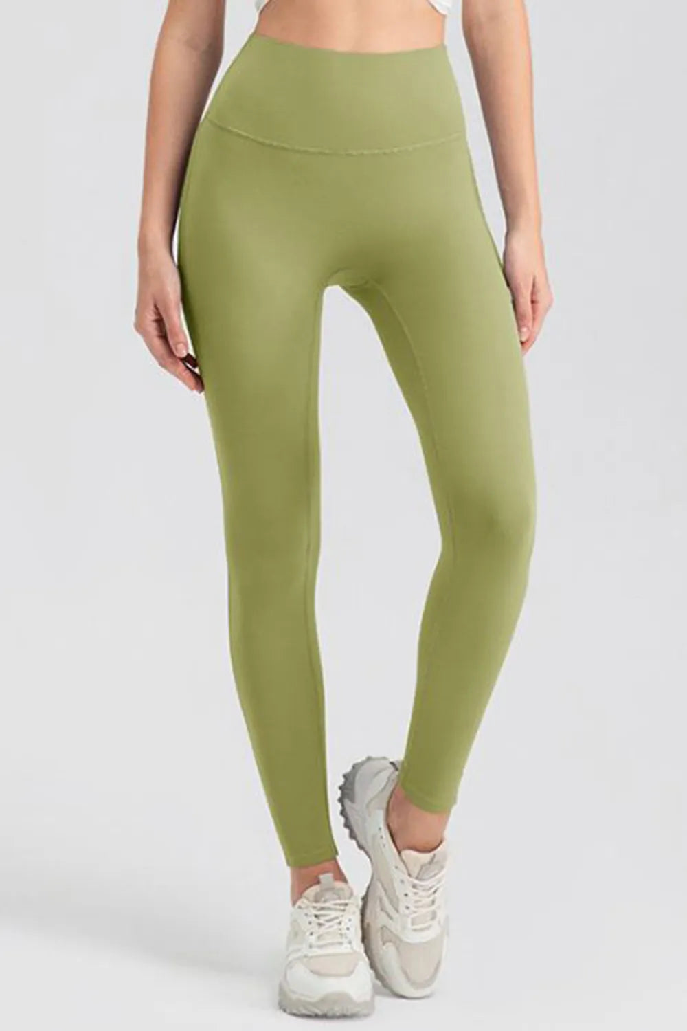 Model wearing olive green high-waist skinny active leggings with a smooth, stretchy fit, ankle-length silhouette, and crossed-leg pose.