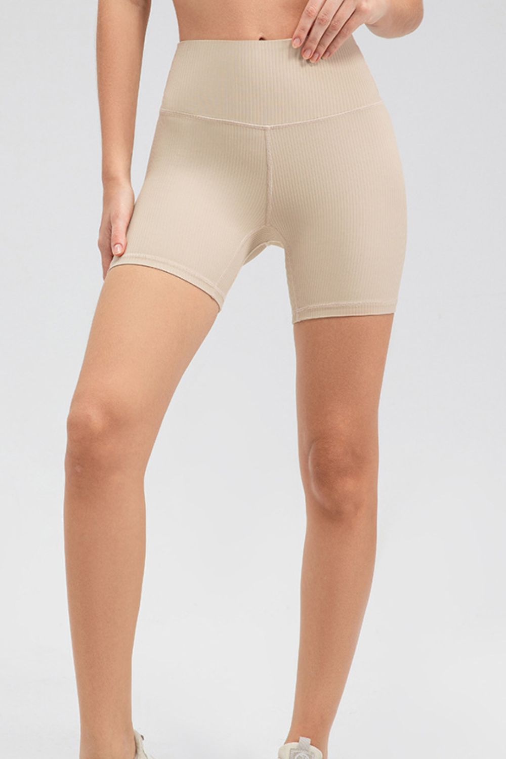 Model wearing solid beige slim-fit sports shorts with a wide waistband, ribbed texture, fitted mid-thigh silhouette, and visible front seam.