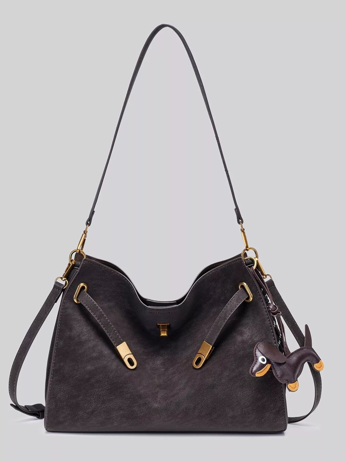 Medium dark brown suede crossbody bag with a structured silhouette, long adjustable strap, decorative buckle accents, and gold-tone hardware.