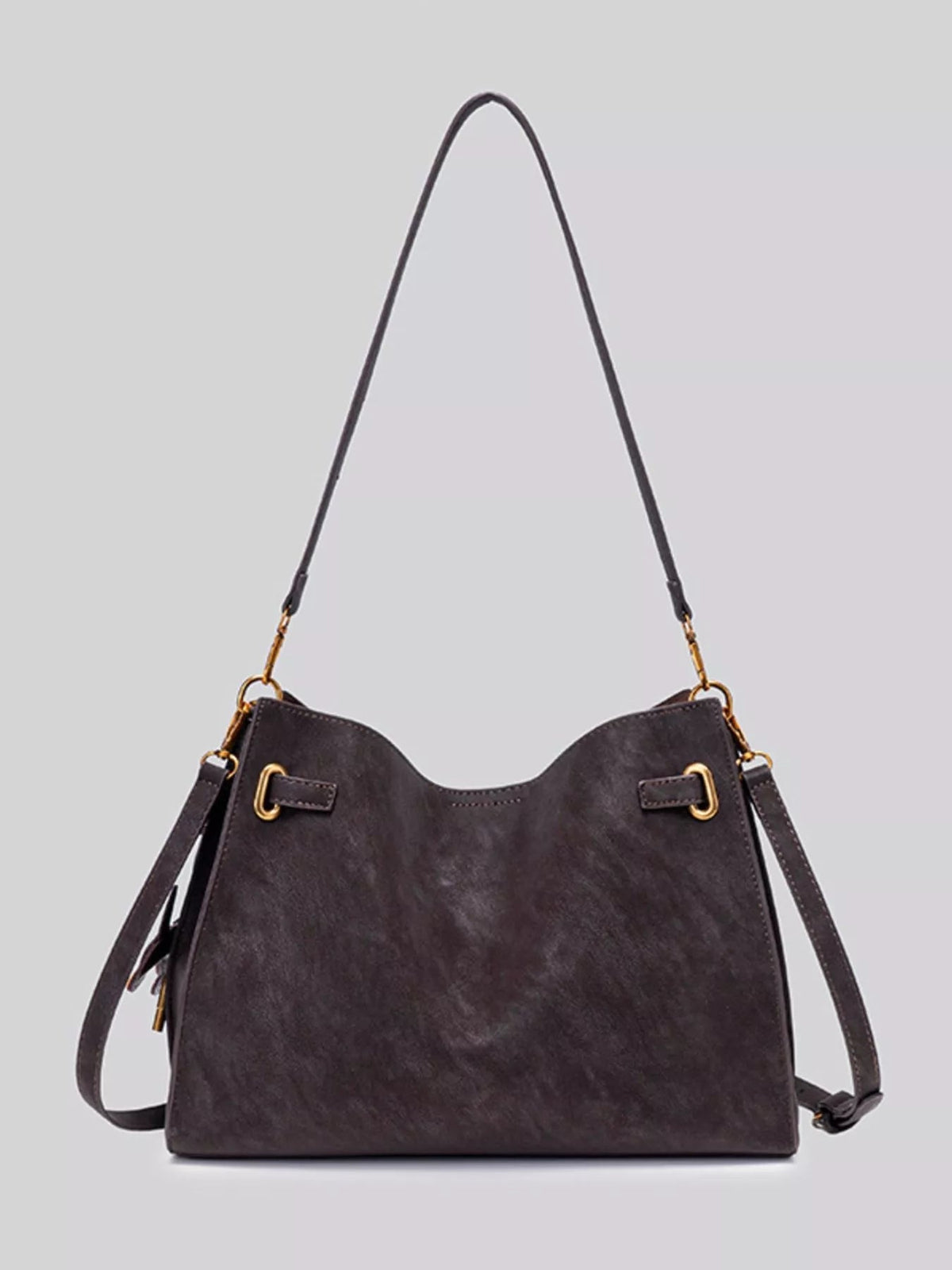 Medium dark brown suede crossbody bag with a wide silhouette, curved top, decorative gold buckles, stitched edges, and a long adjustable strap.