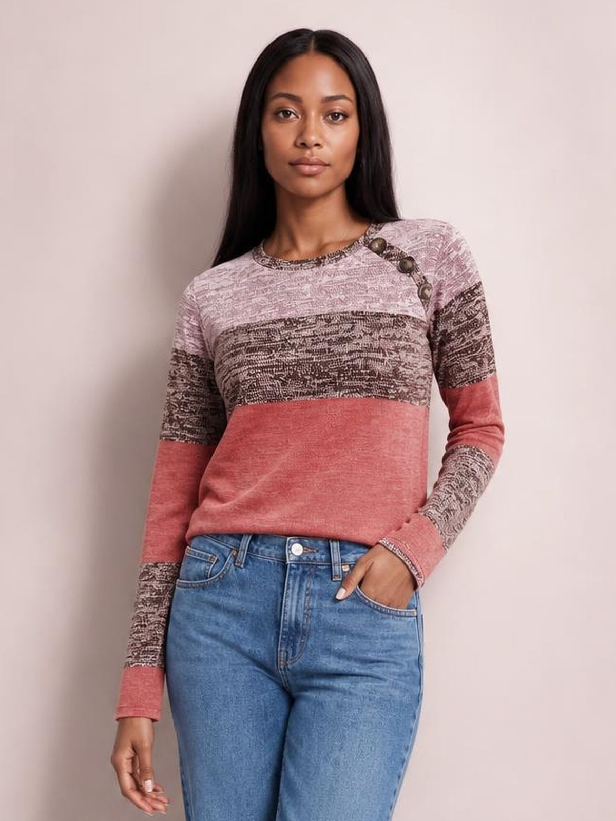 Model wearing a pink and patterned contrast round-neck long-sleeve T-shirt with decorative shoulder buttons and a relaxed silhouette, posing with one hand in her jeans pocket.