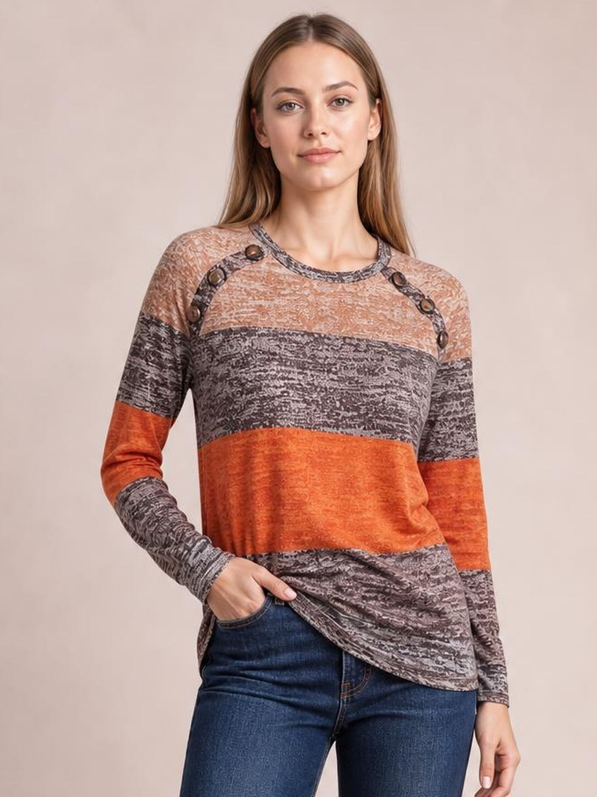 A model poses in a long-sleeve t-shirt with a round contrast neckline, decorative buttons, gray and rust color-blocked construction, and a curved hem.