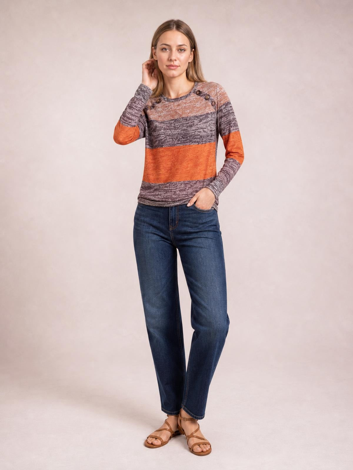 A model poses in a relaxed-fit, round-neck long-sleeve T-shirt with gray and orange contrast bands, textured fabric, and decorative shoulder buttons.