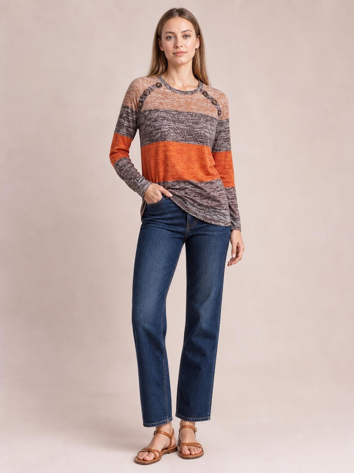 Model poses with one hand in her jeans pocket, wearing a color-block contrast round-neck long-sleeve T-shirt with decorative shoulder buttons and a relaxed silhouette.