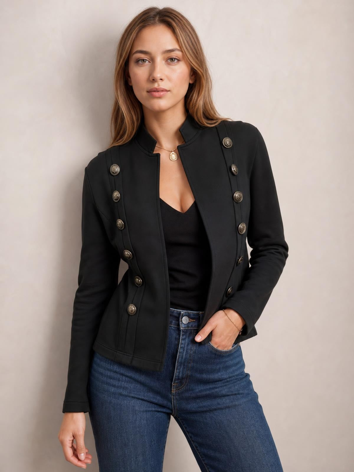 Model wearing a black open-front long sleeve jacket with a structured silhouette, decorative buttons, and vertical seam detailing, posed with one hand in her jeans pocket.