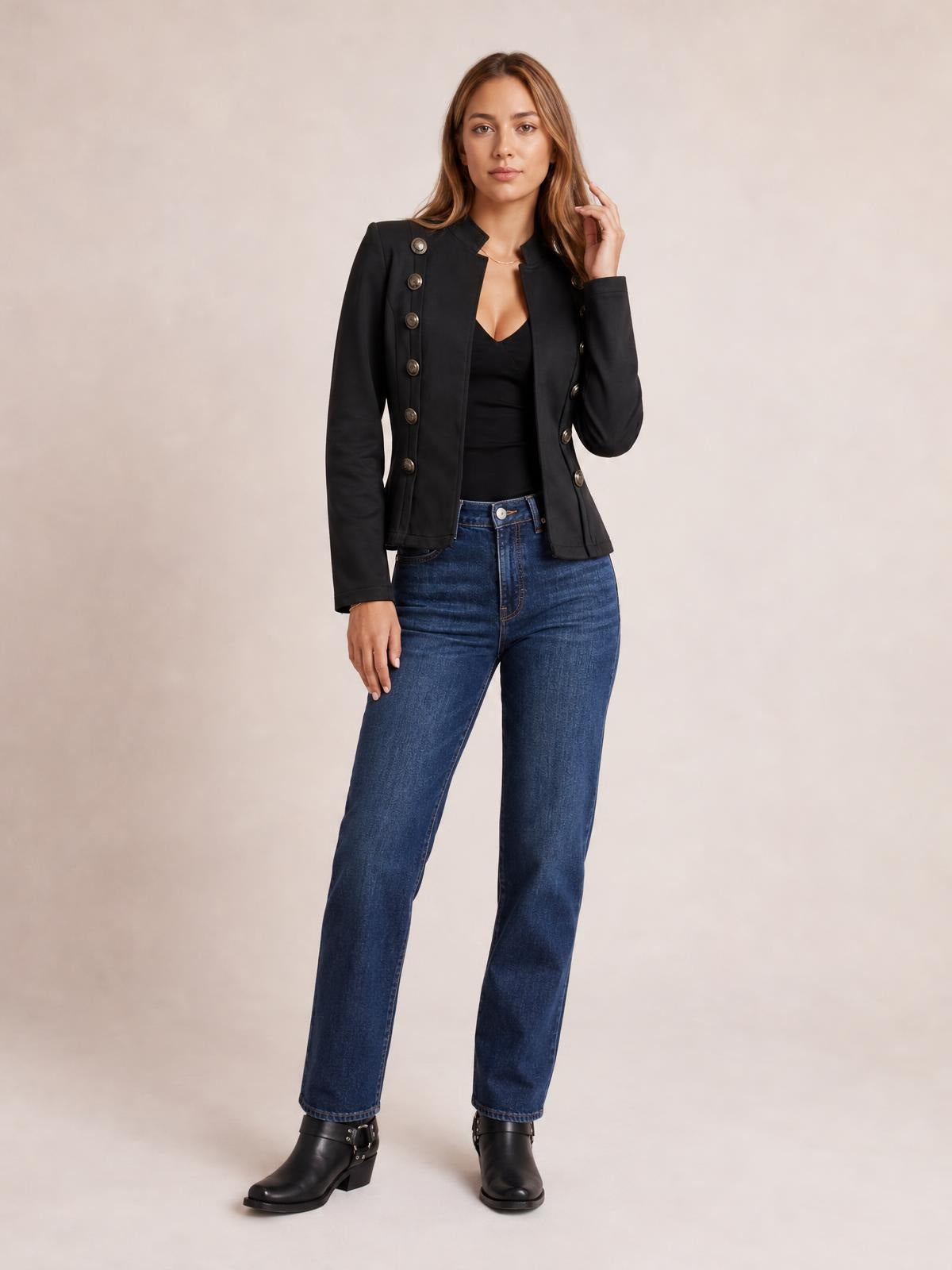 A model poses in a black open-front long-sleeve jacket with decorative buttons, a fitted silhouette, structured shoulders, and a slightly flared hem.
