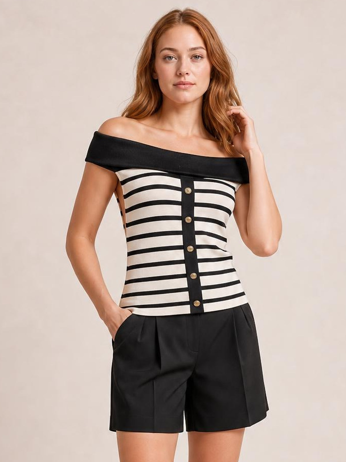 A model poses in a fitted black-and-cream striped knit top with an off-shoulder neckline, black trim, and a row of decorative buttons.
