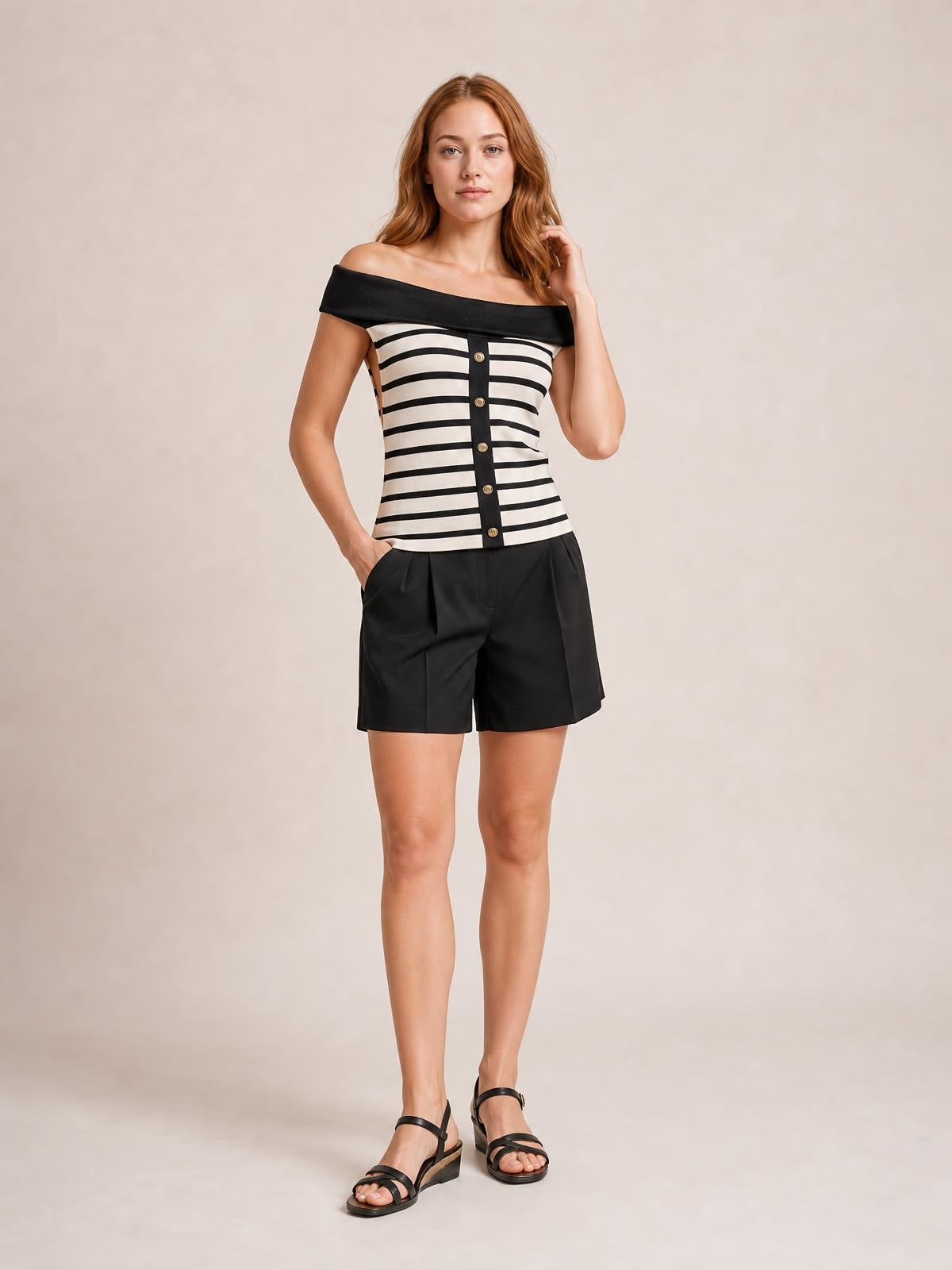 Model poses in a black-and-white striped knit top with an off-shoulder neckline, fitted silhouette, and decorative button placket.
