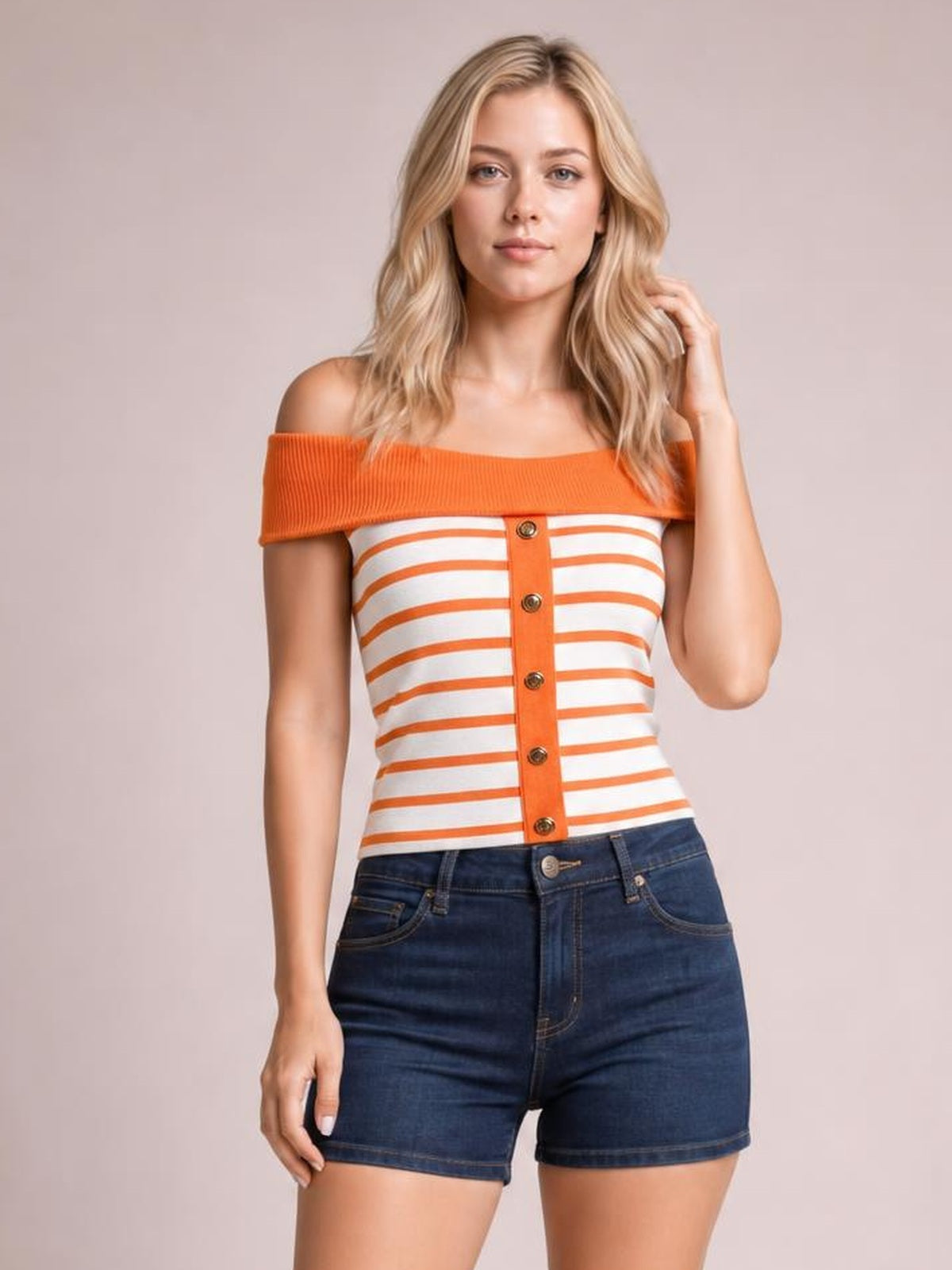 Model wearing an orange and white striped knit top with an off-shoulder neckline, fitted silhouette, and decorative button placket, posing with one hand in her hair.