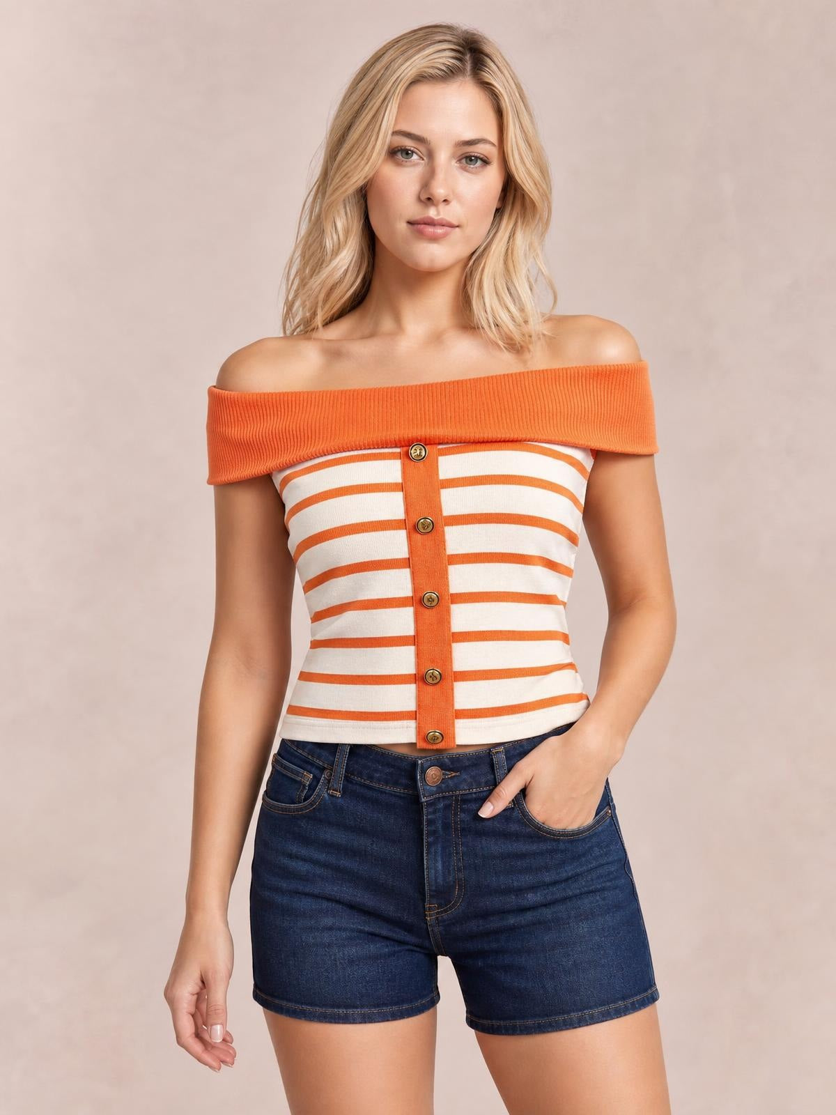 Model poses in an orange-and-white striped off-shoulder knit top with a fitted cropped silhouette and decorative front buttons, one hand in her pocket.